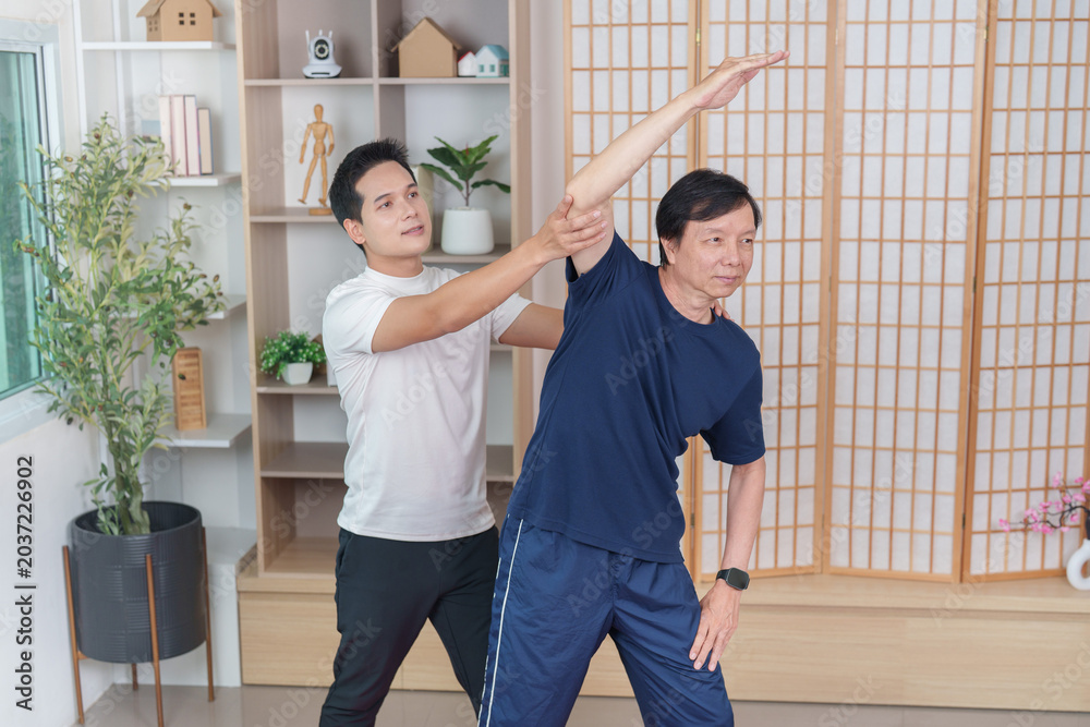 Obraz premium Asian man assisting senior with stretching exercise at home