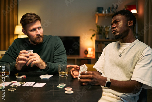 Foto Young adult Caucasian man and Black man playing poker, bluffing and reading each other during home game, expressing male friendship and leisure