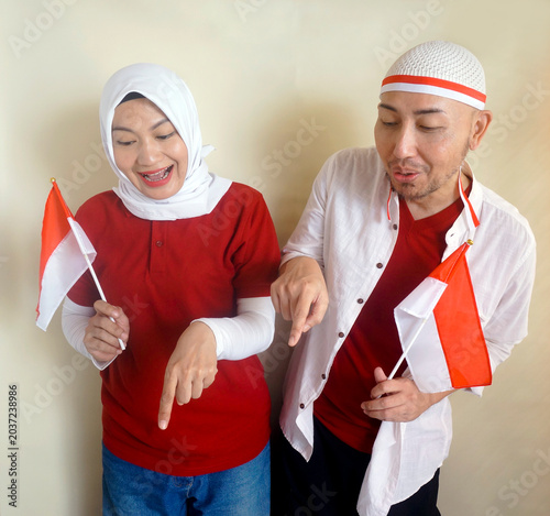 Asian Couple Pointing Down To Copy Space For Text Or Ads While Holding Little Flag. Independence Day Celebration And Supporter Concept