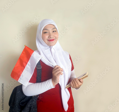 Young Female Student Holding Indonesian Little Flag and Books Shows Support For National Football Team. Sports, Fan and Celebrating Independence Day Concept 