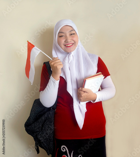 Happy Asian College Girl Holding Indonesian Flag And Books Showing Support For Her Football Team. Sports, Fan And Independence Day Celebration