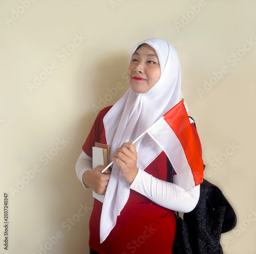 Side View Of Young Girl Wear Hijab And Backpack Looking Away While Holding Flag And Books