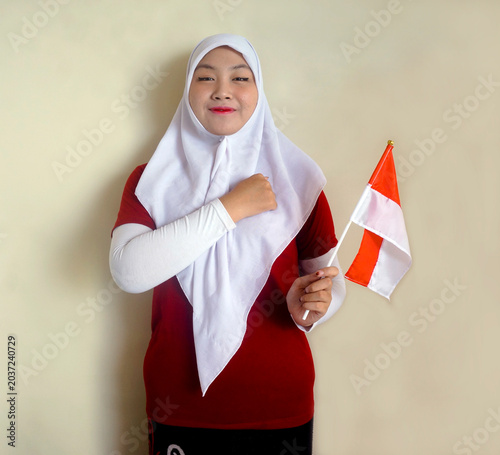 Closeup Of Young Girl Put Hand On Chest Showing Respect While Holding Indonesian Flag. Education, Football Fan and Independence Day Concept