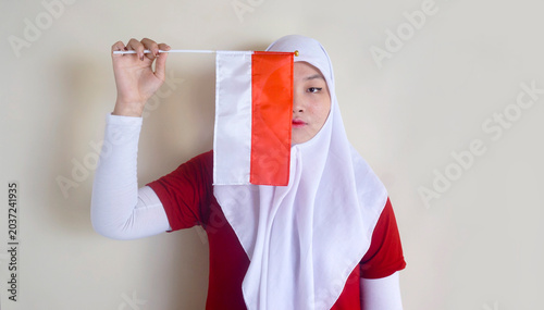 Indonesian Woman In Hijab Holding Little Flag To Covering Her Face. Concept Of Independence Day And Football Fans