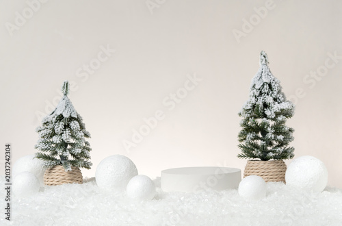 Canvastavla Minimal Christmas product display scene featuring a white cylindrical podium surrounded by real snow-covered pine trees, white ornament balls, and artificial snow on a neutral studio background