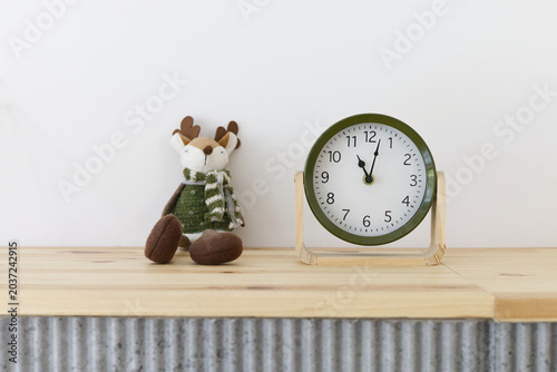 Cute plush toy deer in green sweater and scarf and simple, green clock on the wooden counter