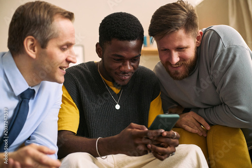 Schilderij op canvas Multiethnic young adult men gathering around smartphone, sharing content and smiling, expressing male friendship and connection