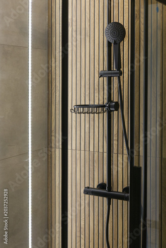 Horizontal view of a modern, black shower, wood-like long tiles on the wall lit by the long, white LED stripe