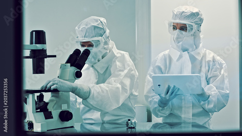 Foto In a sterile laboratory, two researchers clad in clean suits meticulously examine samples under microscopes, exemplifying advanced biotechnology and medical research efforts