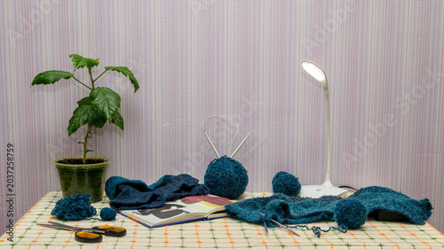 knitting supplies with blue wool and an open book on a table in the room