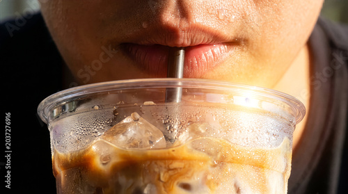 Extreme macro close up of sweaty mouth drinking iced latte coffee through straw from condensation covered cup.