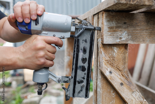 Tableau sur toile A person uses a pneumatic brad nailer to assemble a weathered wooden frame struc