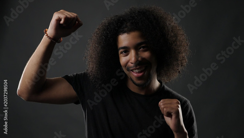 Foto Happy mixed race man with curly hair cheering, expressing joy against a dark bac