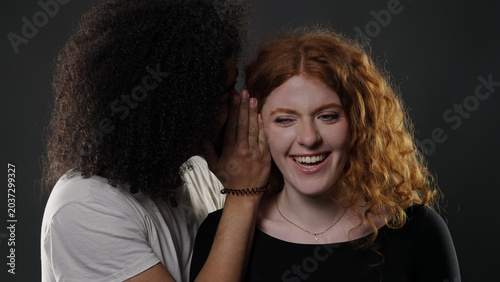Foto Diverse couple sharing secret, whispering into ear, laughing happily, showing in