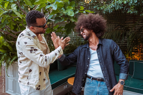 Two smiling latin american men high fiving, celebrating friendship and achievement in a lush outdoor setting.