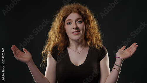 Fotografía Young woman with red hair raising hands, unsure and hesitant on dark background