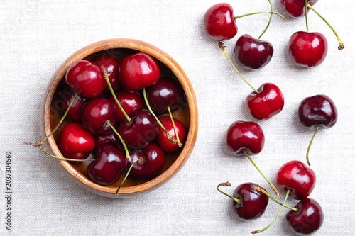 Fresh cherries in a wooden bowl on linen. Ready to eat, red and ripe fruits of the true cherry species Prunus avium, a stone fruit cultivar of the variety Royal Ruby 7. Close-up, from above. Photo