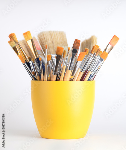 Artist paint brushes in a yellow flower pot. Mix of new and used artist brushes, in various sizes and widths, some made of synthetic hair and some of natural bristles. Front view over white. Photo