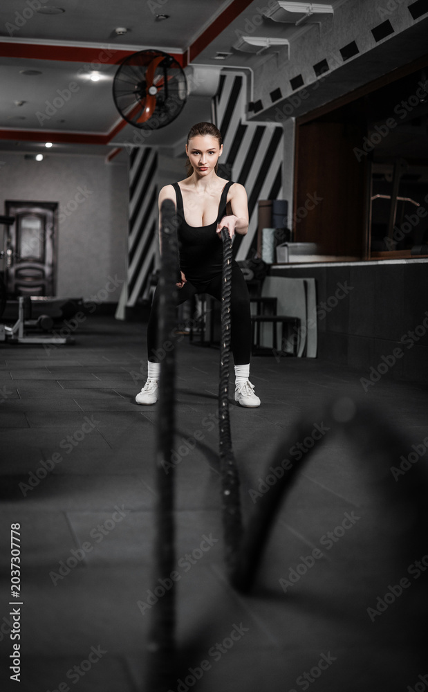 Obraz premium A beautiful girl training with a CrossFit rope in the gym.