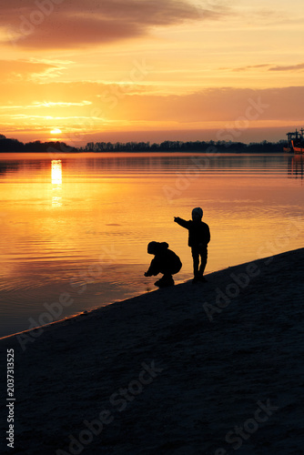 Children silhouettes playing peacefully beside lake during golden sunset evening
