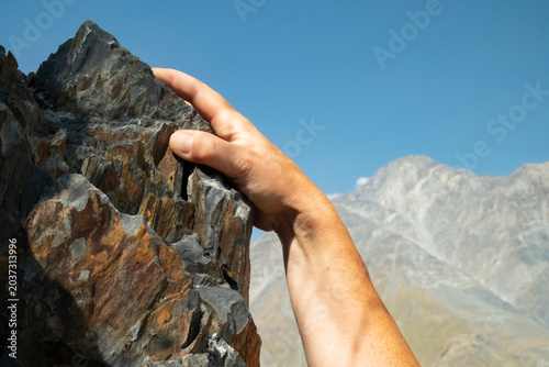 Konstfotografi Climber reaches for a rock ledge on a mountain during daytime in a rugged outdoo