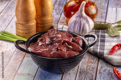 Quadro su tela Raw chicken liver in a black bowl with garlic, chili, and spices on a rustic wooden table