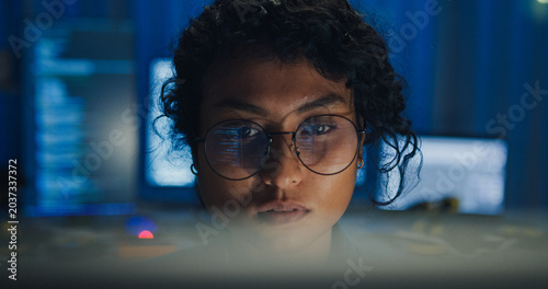 Close-up Black female programmer with code reflection in glasses working late in home office at night. Cybersecurity, AI algorithm, Network security, software developer, serious face, burnout concept.