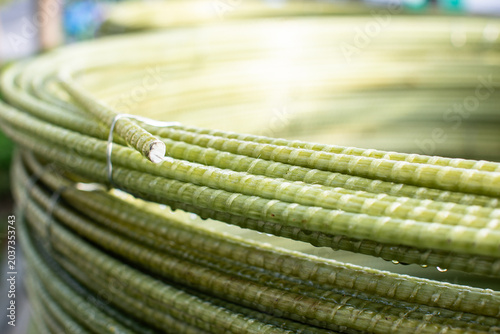 Coiled coils of greenish fiberglass rebar (GFRP) stacked on a city sidewalk. The lightweight, ribbed composite material is bundled with wire, showing a modern alternative.