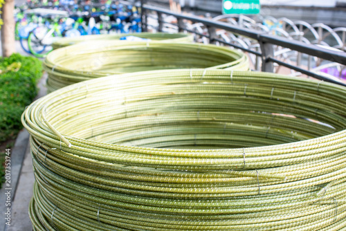 Coiled coils of greenish fiberglass rebar (GFRP) stacked on a city sidewalk. The lightweight, ribbed composite material is bundled with wire, showing a modern alternative.