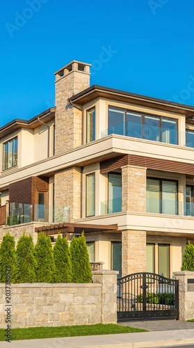 Luxurious Modern Home with Stone Facade and Black Gate Under Clear Blue Sky.