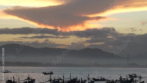 Scenic sunrise over Papuma Beach harbor with silhouettes of traditional fishermen boats floating on misty sea, Jember.