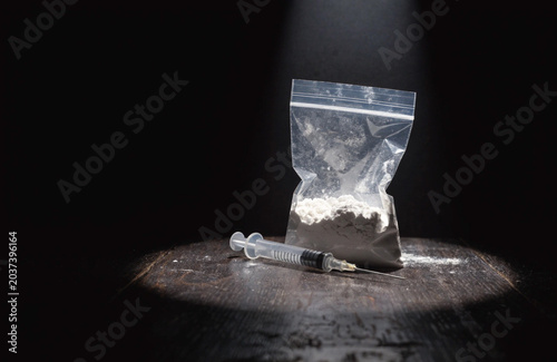 Syringe and Bag of White Powder on Table Under Spotlight Symbolizing Drug Use and Addiction