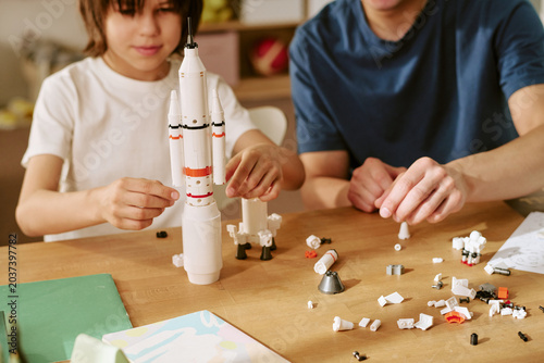 Asian father and child son assembling rocket model at table, learning through play and building STEM skills. Useful for parenting, family bonding, education, innovation campaigns