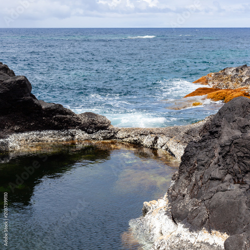 Natural volcanic pools by the ocean on Sao Miguel Island. Rocky coastline meets the sea at Mosteiros. Scenic view of the Atlantic Ocean and rugged shore.