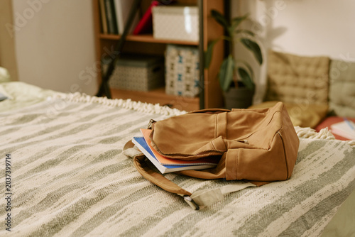Close up of school backpack resting on bed with notebooks visible, suggesting student routine and home study preparation. Useful for education, back to school, parenting campaigns
