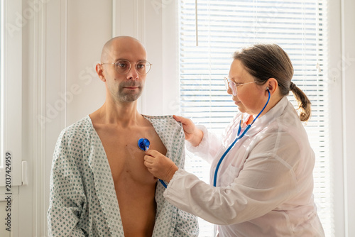 Billede på lærred female doctor using stethoscope listen male patient's chest, doctor performing a
