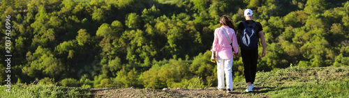 Konstfotografi Rear back view of young couple hikers with backpacks rucksack holding hands and