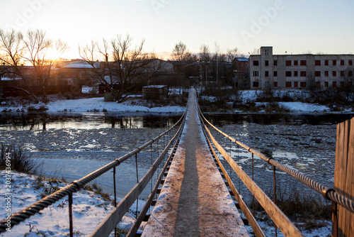 A suspension bridge over the Msta River in winter, on a sunny day. Borovichi, Novgorod Oblast, Russia.