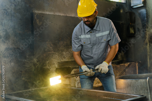 Foto Industrial technician in hardhat using metal tongs to submerge a glowing hot ste