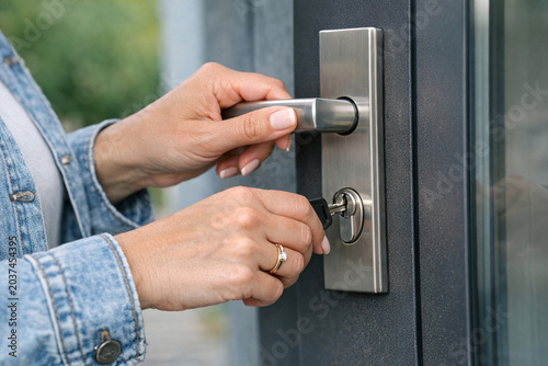 A person with a denim jacket is opening the door with a key.