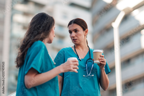 Foto Two female nurses, wearing teal scrubs, having a coffee break outdoors, sharing
