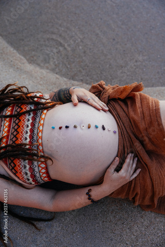 Maternity image of a mother with relaxing stones on her belly near water. 