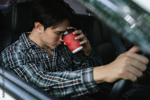 Foto Sleepy driver yawning while holding a coffee cup inside a car, representing driver fatigue, drowsy driving, caffeine consumption, road safety, and commuting stress