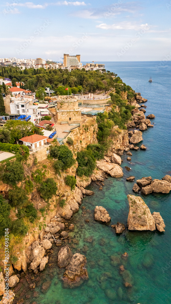 Obraz premium High angle drone view of the historic Hidirilik Tower standing on steep rocky cliffs along the Mediterranean coast of Antalya old town Kaleici, scenic maritime landscape, Turkey