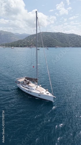 Sailboat glides across calm blue sea with scenic mountains in background