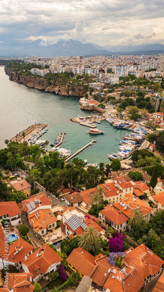 Fototapeta premium drone aerial Antalya old town Kaleici, showing the ancient Roman harbor, traditional red tiled roofs, steep cliffs and modern urban skyline, Turkey