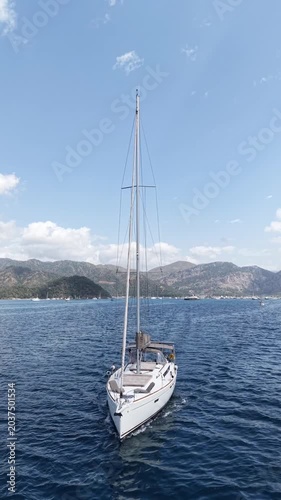 Sailing yachts glide across calm blue waters with scenic mountains in the background