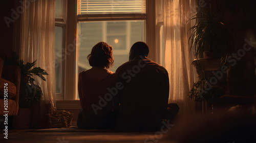 Intimate cinematic interior couple sitting by window at sunset, warm moody lighting, cozy plants and soft curtains