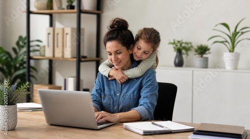 Mother working on laptop with child hugging her