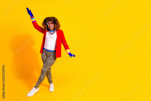 Tablou pe pânză Joyful stylish woman dancing in colorful outfit against bright yellow background